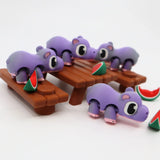 Colorful 3D printed purple hippo sensory toys on picnic tables with watermelon slices.