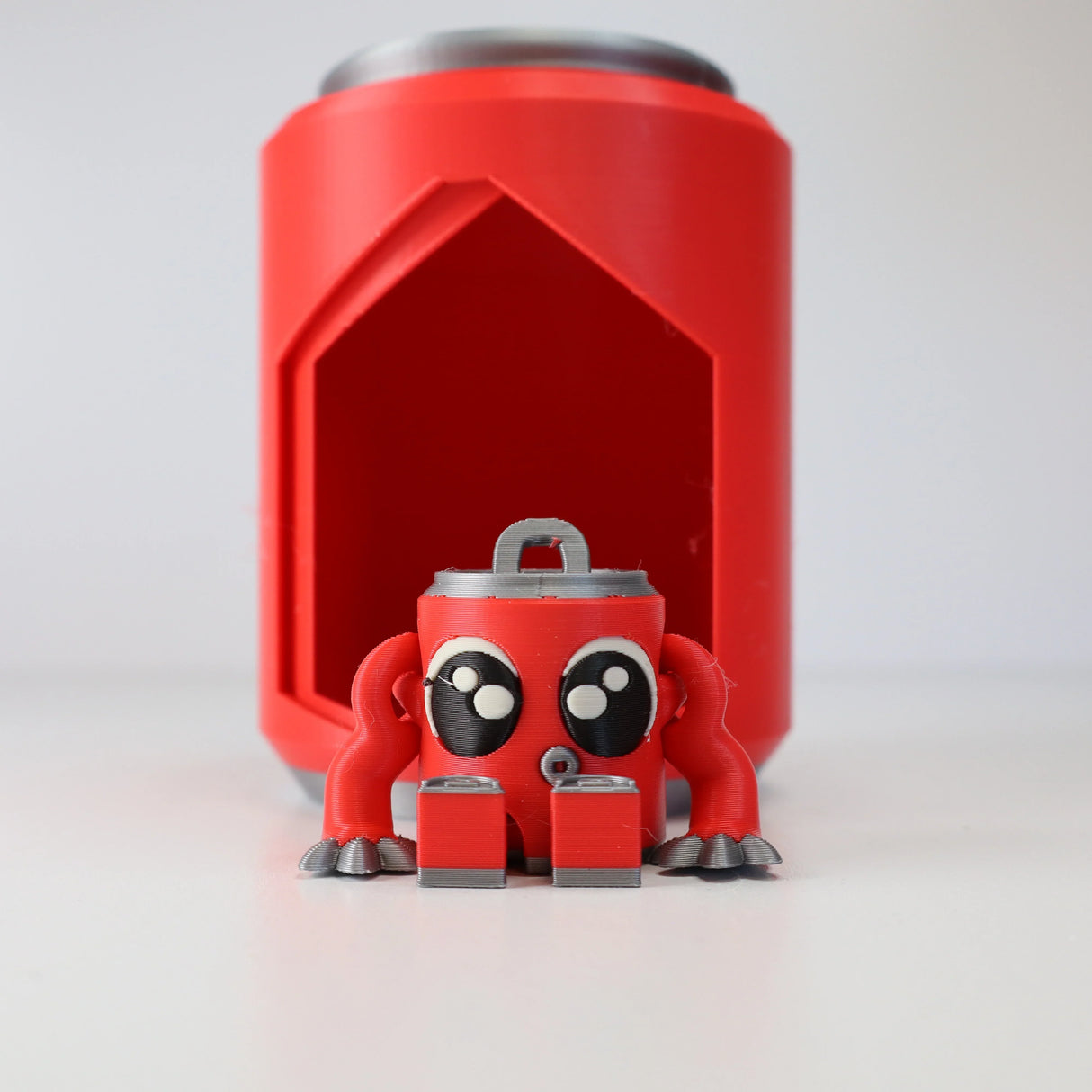 3D printed red sensory toy can with cute eyes and arms in front of matching holder