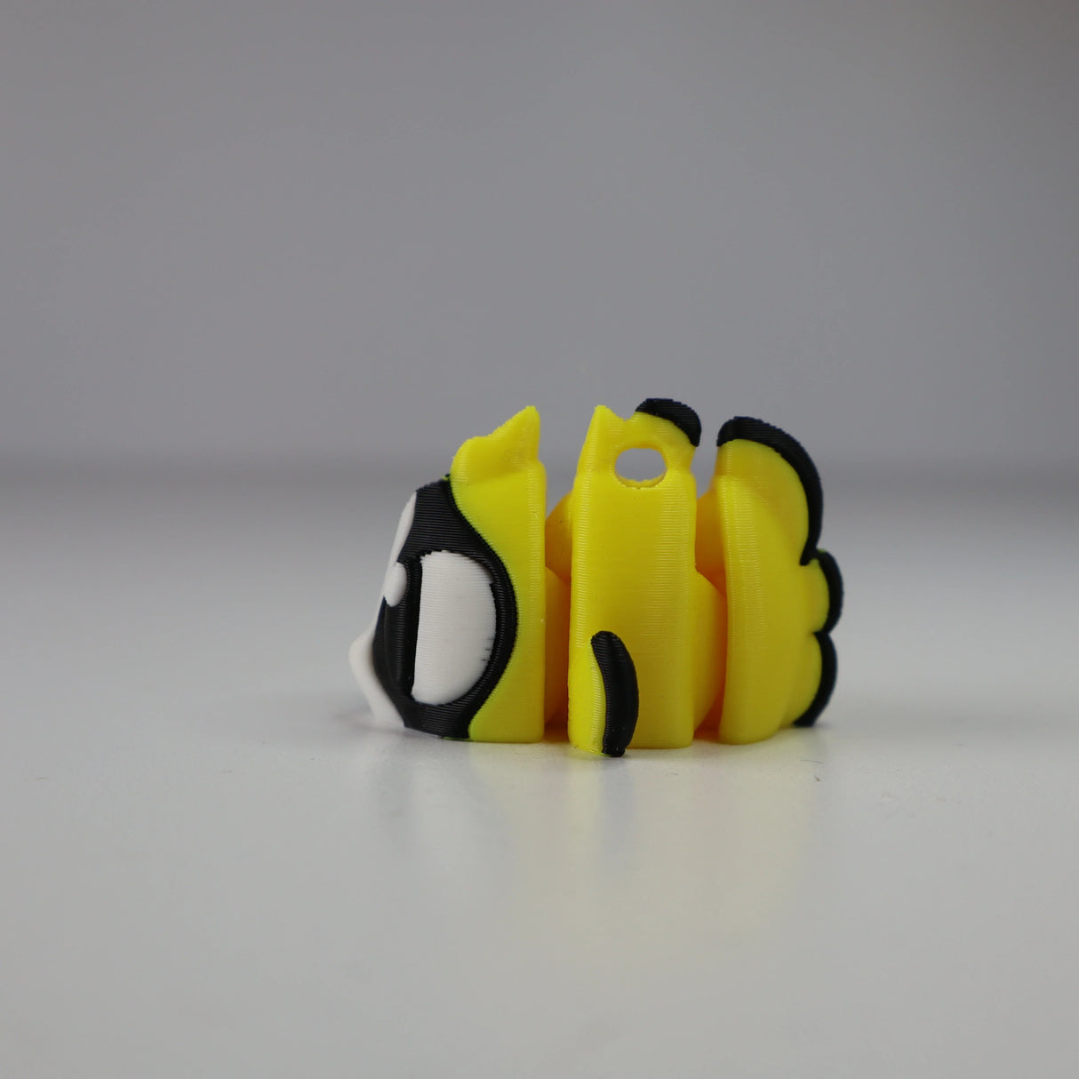 Yellow 3D printed bee sensory toy with black wings and cartoon eyes on a white surface.