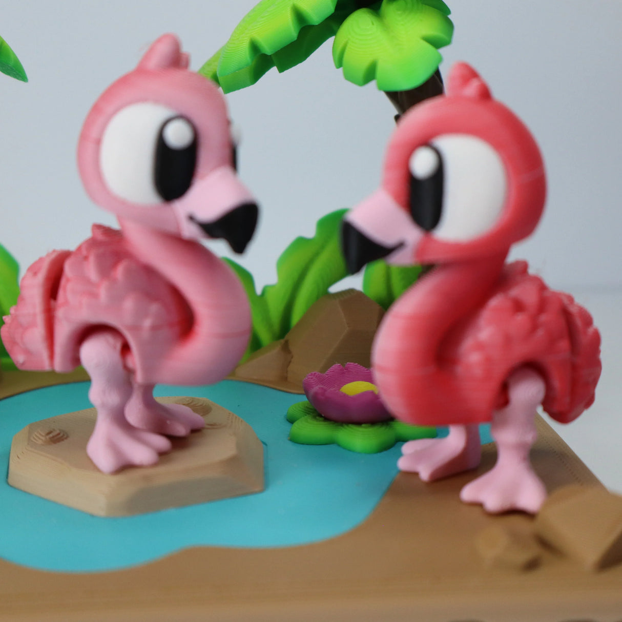 Colorful 3D printed flamingo sensory toys on a tropical playset with water and palm trees