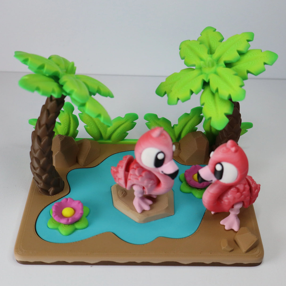 3D printed sensory toy with two pink flamingos, palm trees, and a pond on a colorful base