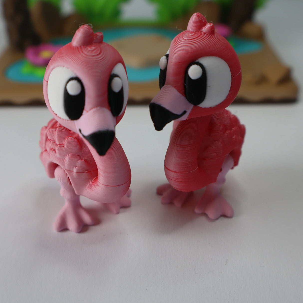 Pair of pink 3D printed flamingo sensory toys with large eyes on white surface