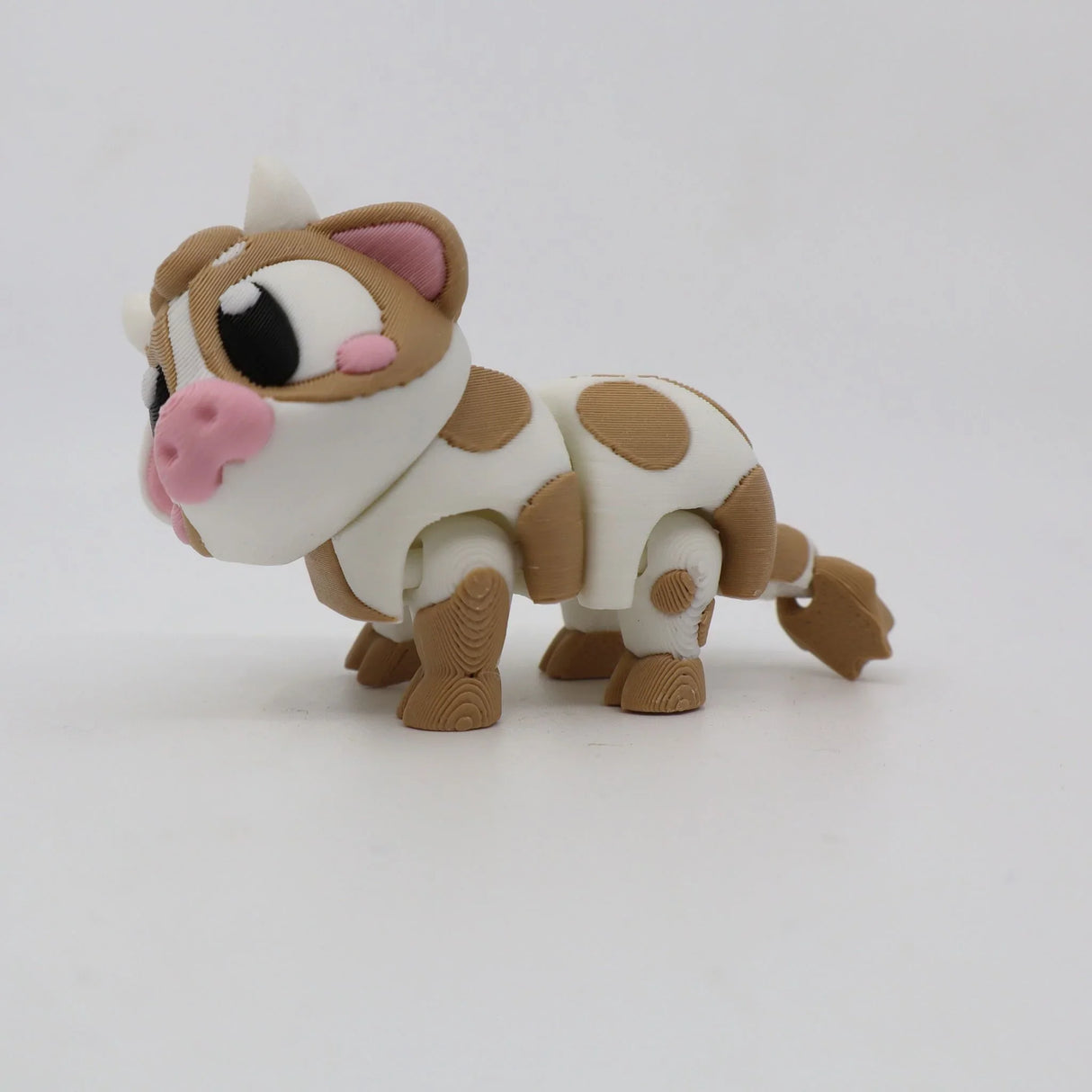 3D printed sensory toy cow with brown spots and pink nose on white background