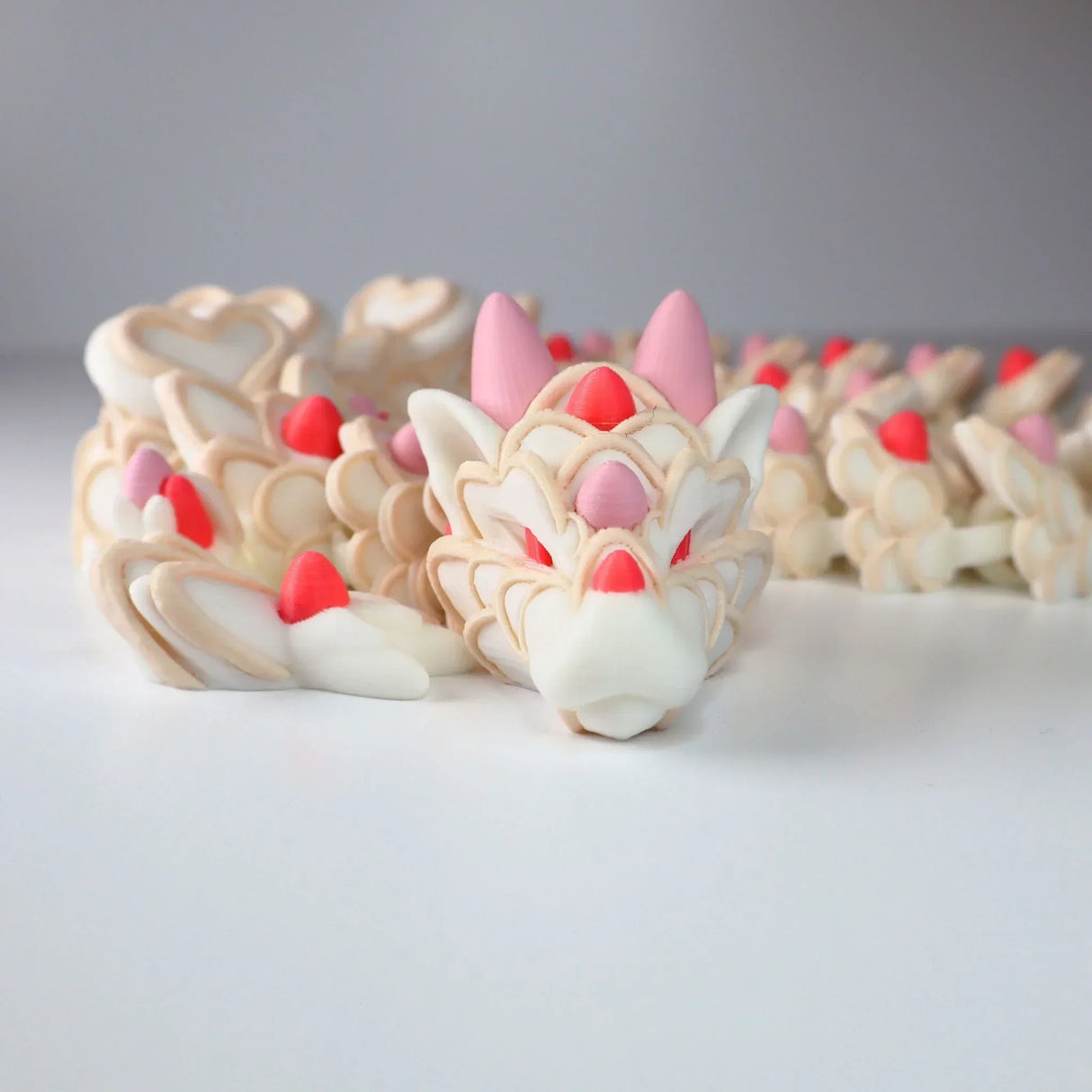 3D printed sensory dragon toy with cream, pink, and red colors on white background