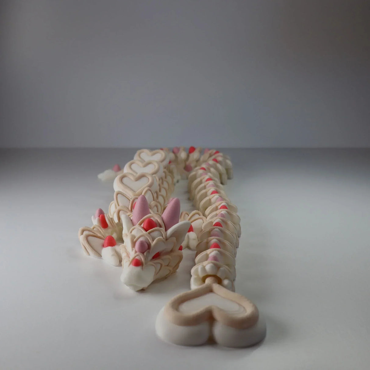 3D printed sensory dragon toy with heart patterns in beige, pink, and red accents