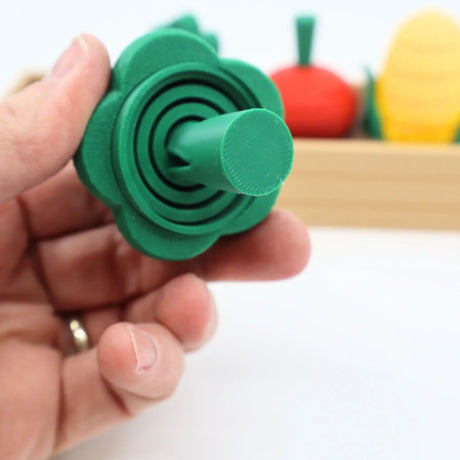 Hand holding green 3D printed sensory vegetable fidget toy with other colorful toy veggies in background