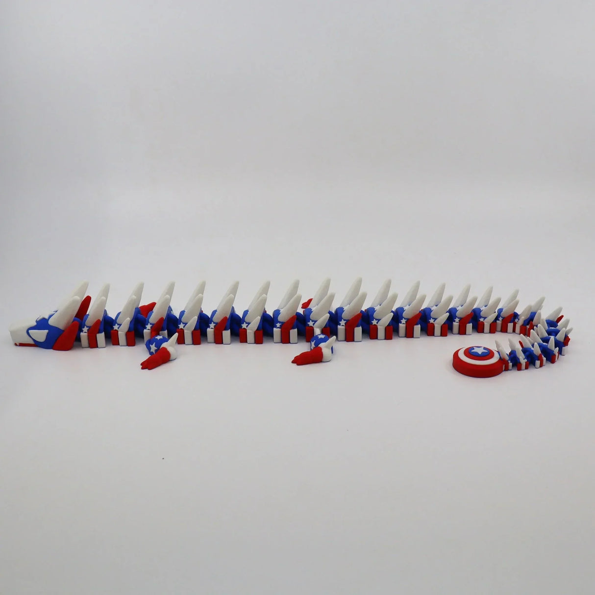 Red, white, and blue 3D printed flexi dragon toy with star pattern and shield, ideal for sensory play