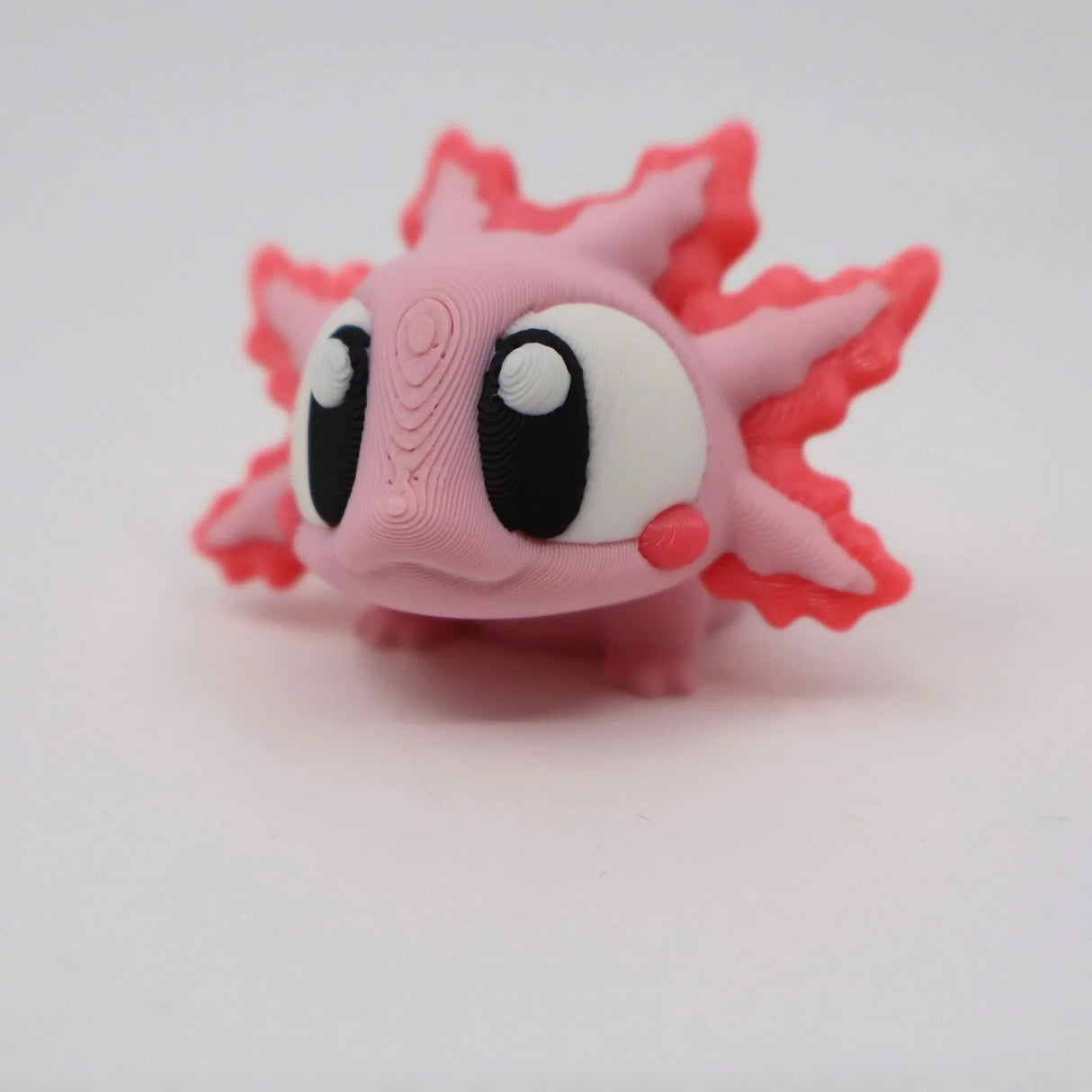 Cute pink 3D printed axolotl sensory toy with large eyes on a white background
