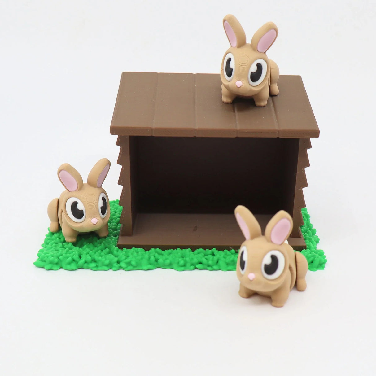 Three cute 3D printed bunny toys with a brown hutch on green textured grass
