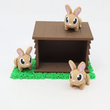 Three cute 3D printed bunny toys with a brown hutch on green textured grass