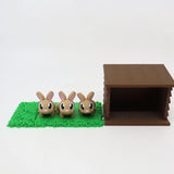 Three cute 3D printed bunny toys on green mat beside brown hutch, sensory educational toy