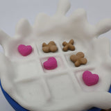 3D printed sensory tic-tac-toe game with heart and X pieces on a white splash-shaped board