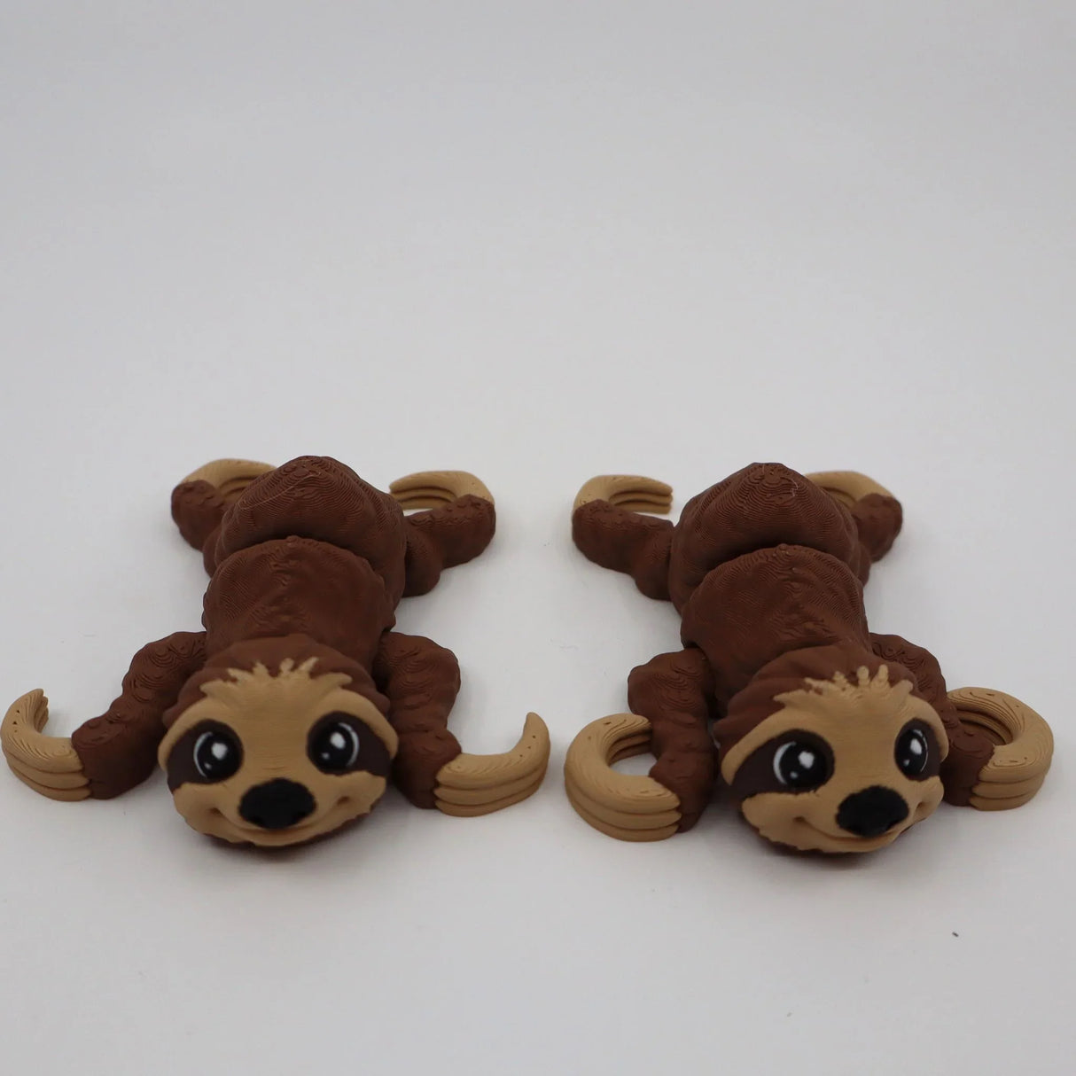Two brown 3D printed sloth sensory toys with big eyes on a white background.