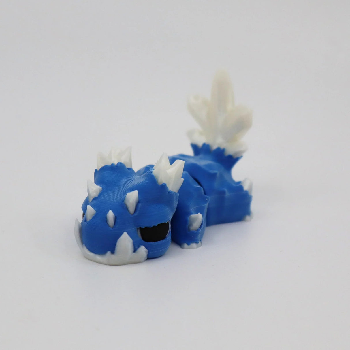 Blue and white 3D printed sensory toy dragon with spikes on a plain background