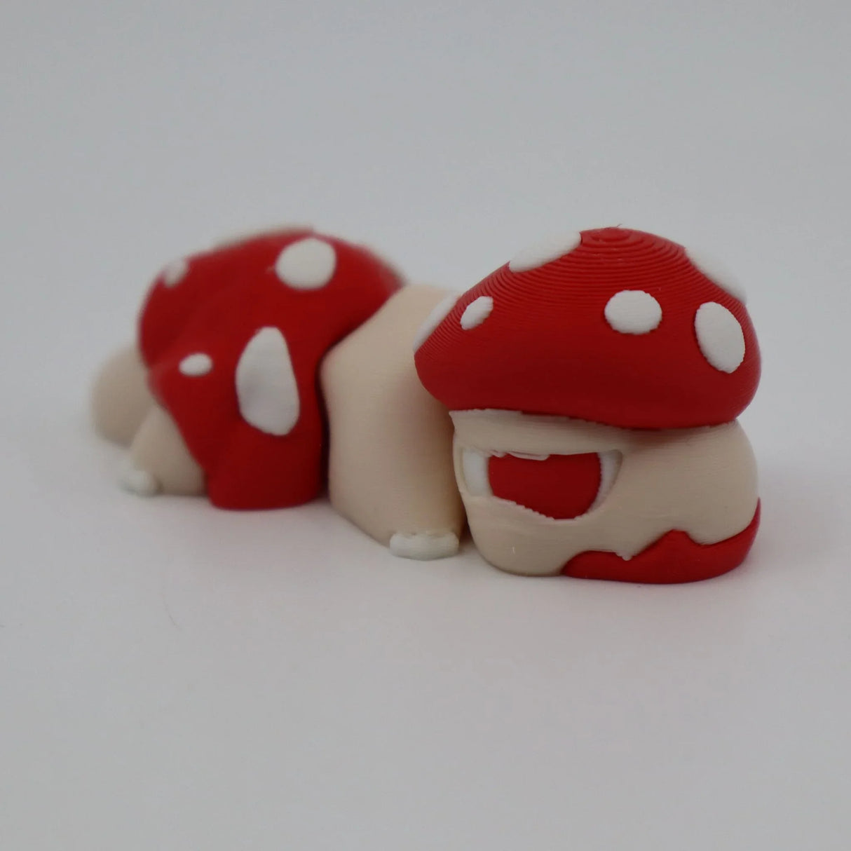 3D printed sensory toy caterpillar with red and white mushroom caps on white background