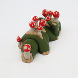 Green 3D printed sensory toy caterpillar with red mushroom details on white background