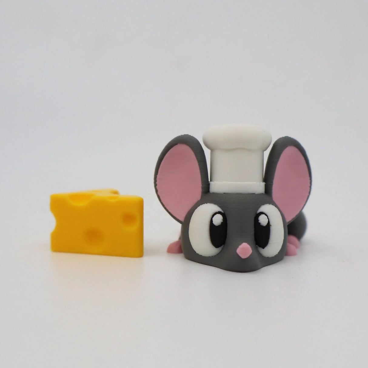 Cute 3D printed mouse toy with chef hat next to a yellow cheese sensory toy on white background