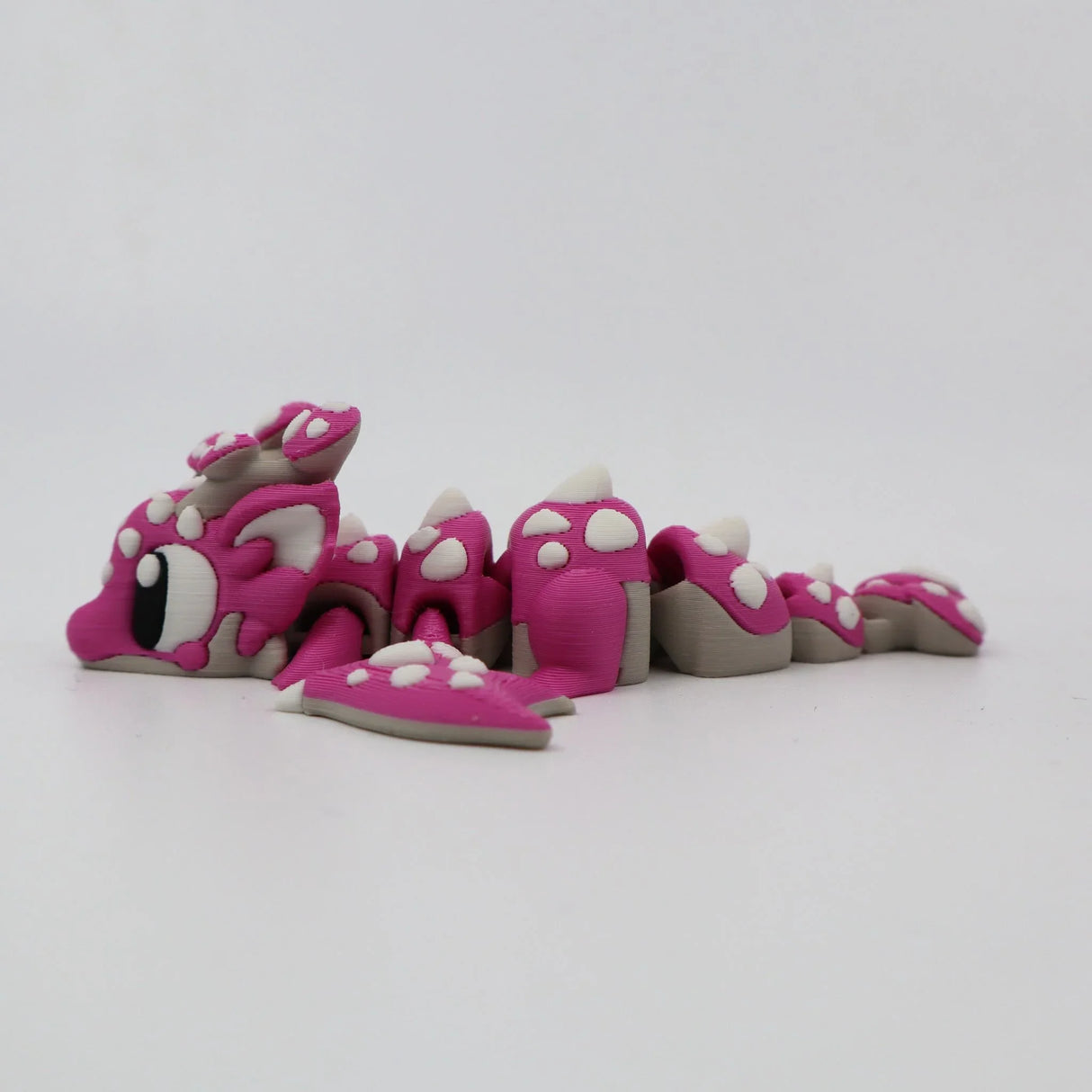 Pink 3D printed flexi dragon fidget toy with white spots, designed for sensory play and tactile stimulation.