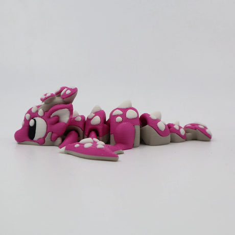 Pink 3D printed flexi dragon fidget toy with white spots, designed for sensory play and tactile stimulation.