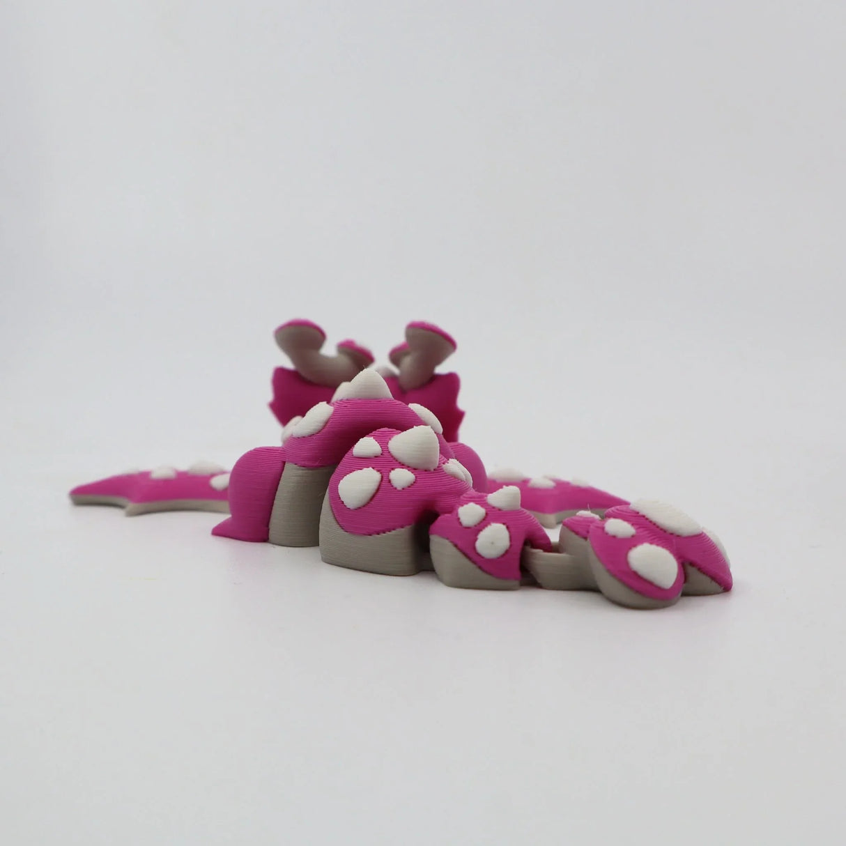 Pink 3D printed flexi dinosaur toy with white spikes, sensory fidget for kids