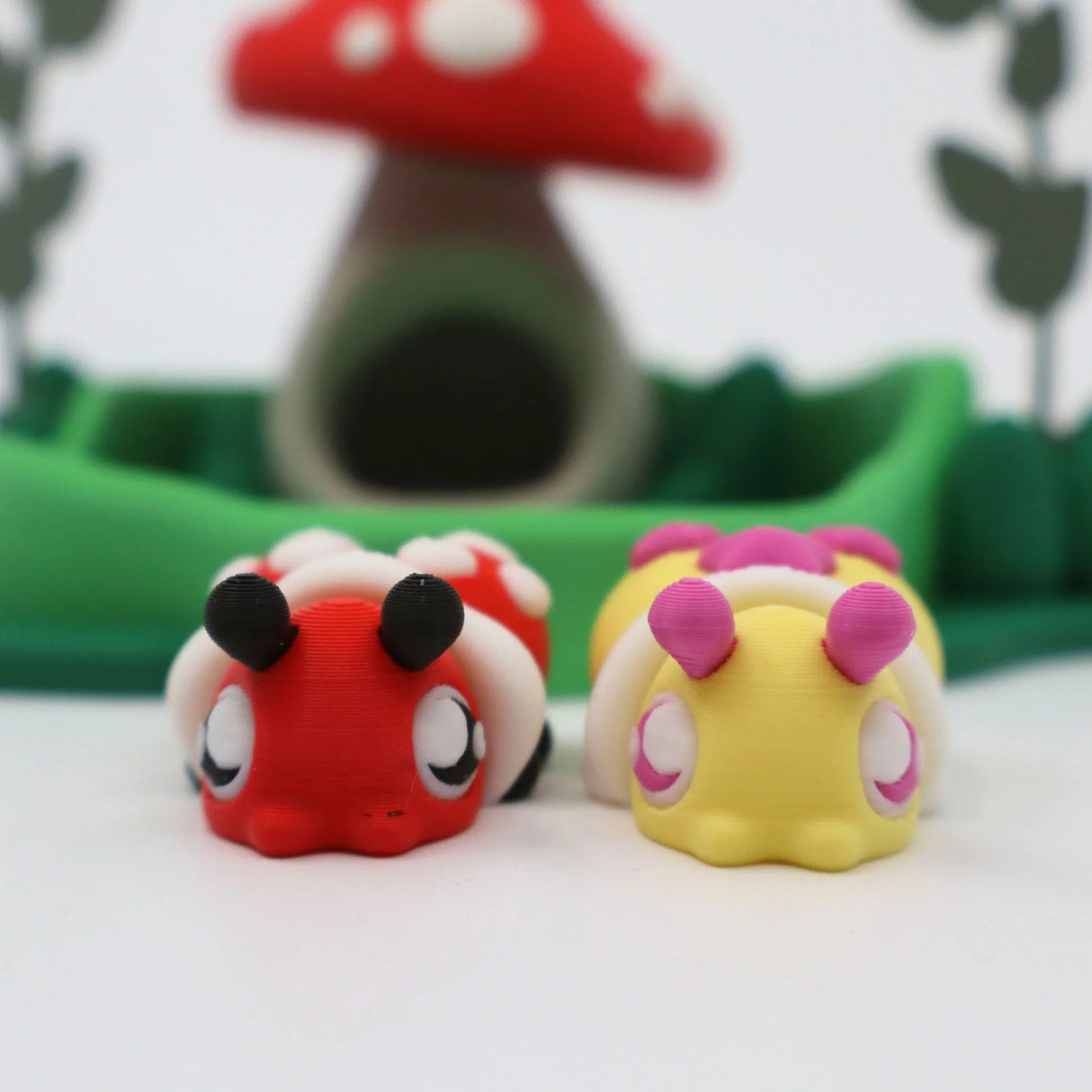 3D printed sensory toy bugs in front of a whimsical mushroom house and green landscape