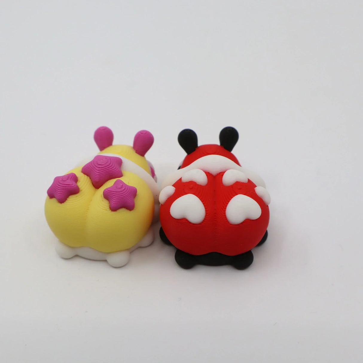Two colorful 3D printed sensory bug toys with heart and star shapes on a white background