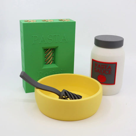 3D printed toy pasta set with green pasta box, white sauce jar, yellow bowl, and utensil