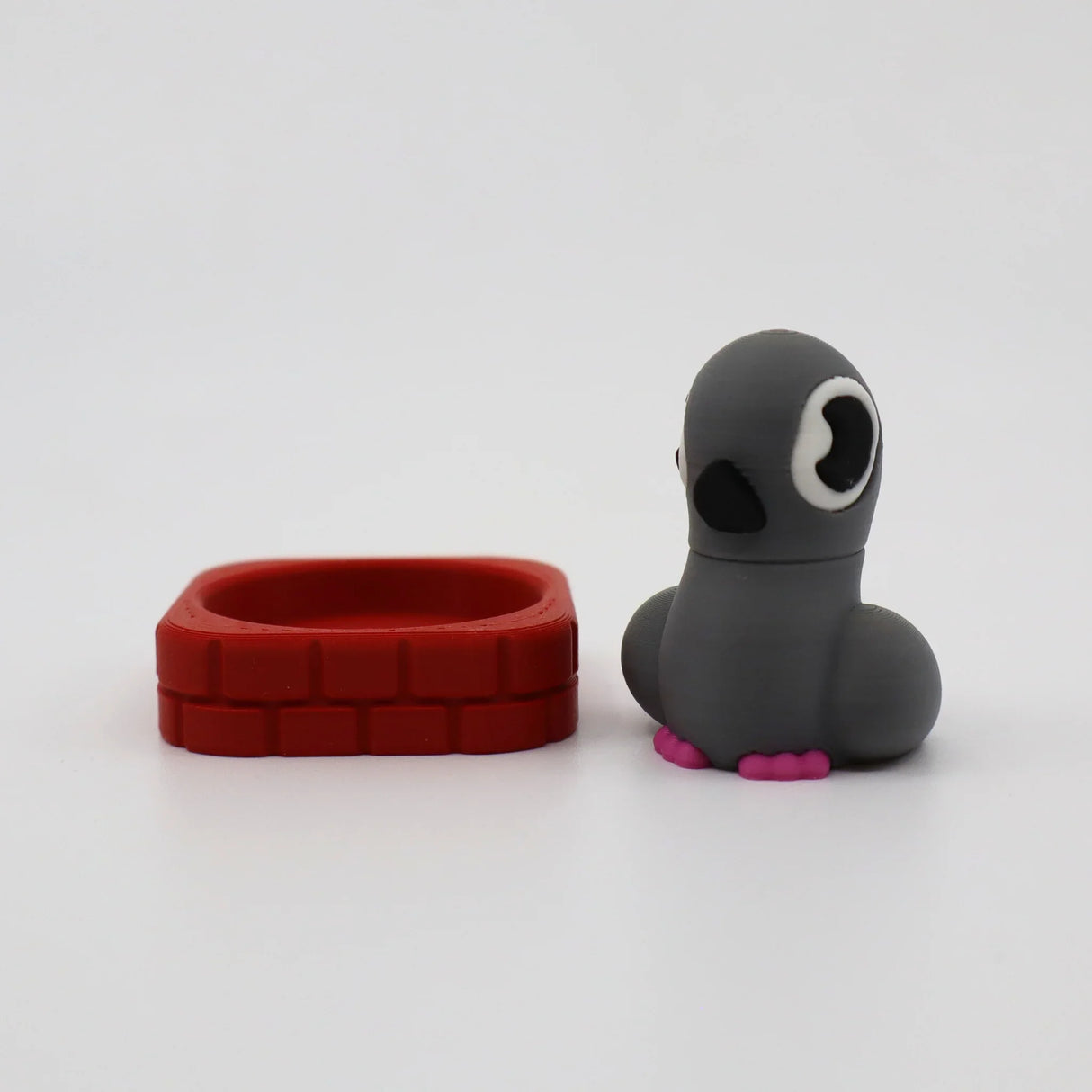 Gray 3D printed fidget toy with pink feet beside red brick-style sensory ring for tactile play