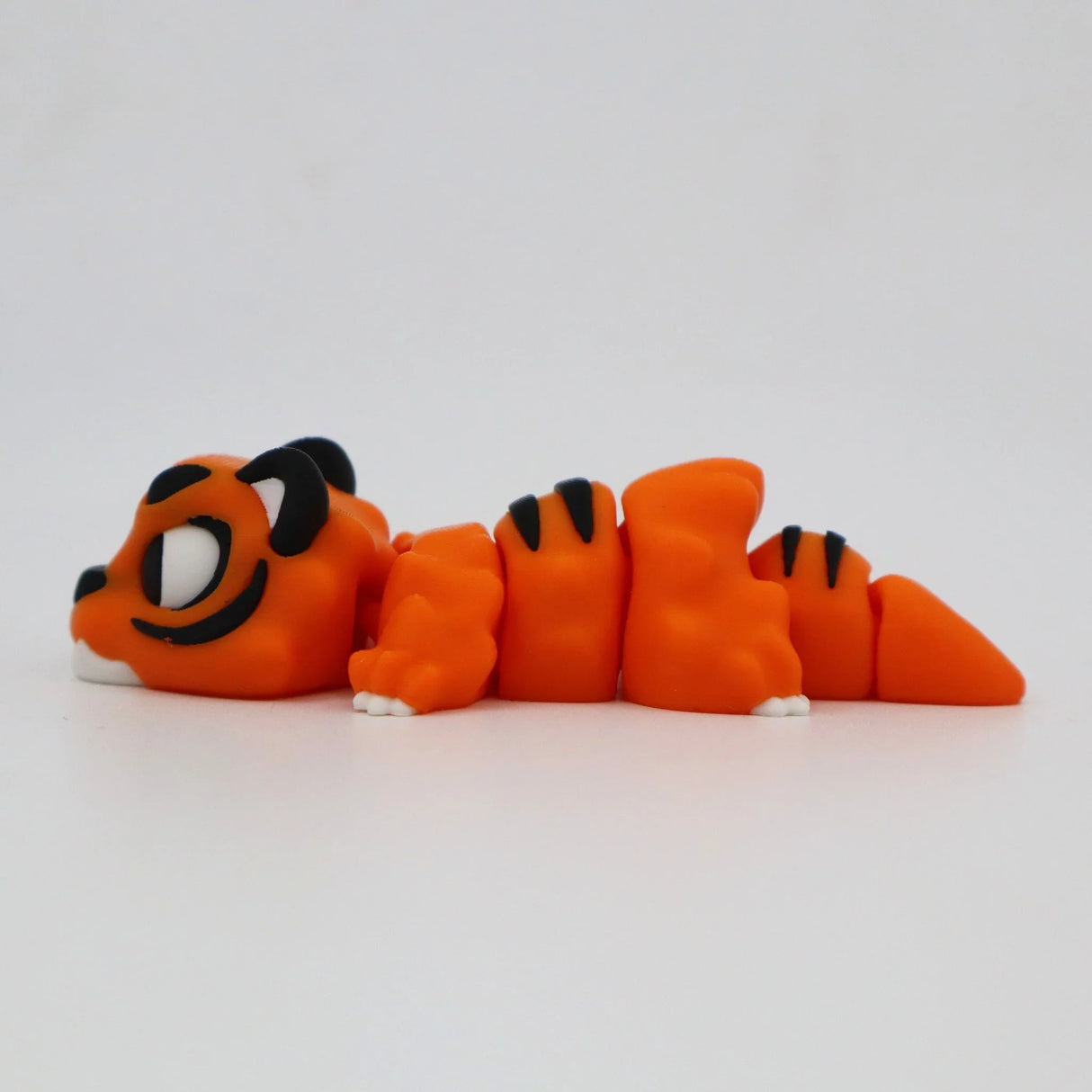 Orange 3D printed tiger sensory toy with black stripes and white accents, laying on side