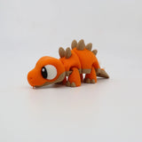 Orange 3D printed stegosaurus sensory toy with movable legs and cartoon eyes on white background