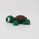 Green and brown 3D printed turtle sensory toy with large eyes on white background.